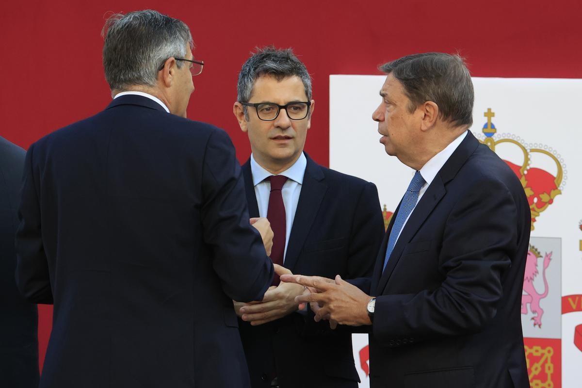 El ministro de la Presidencia, Relaciones con las Cortes y Memoria Democrática, Félix Bolaños (c), conversa con el titular de Agricultura, Luis Planas, mientras aguardan el inicio del desfile del Día de la Fiesta Nacional, este miércoles, en Madrid.