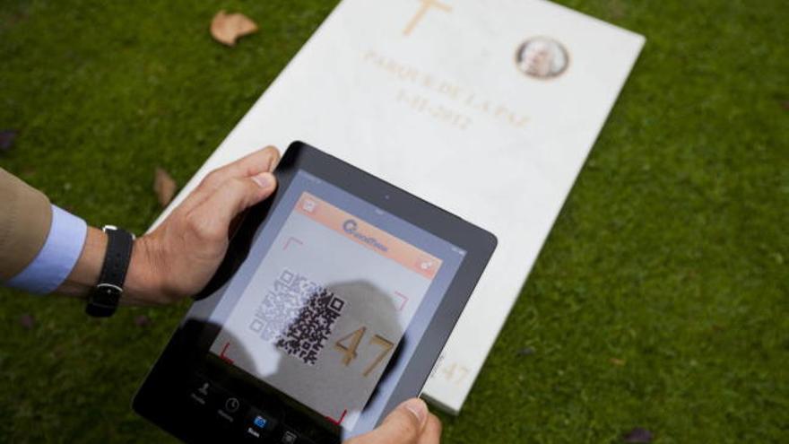 Un hombre lee con su tableta el código QR impreso en una de las lápidas del cementerio Parque de la Paz de Chiva.