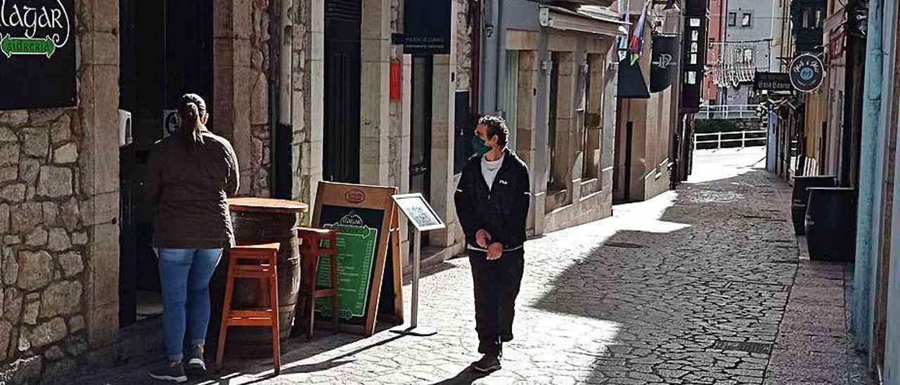 Dos vecinos, ayer, en la calle Manuel Cué de Llanes, zona de sidrerías, donde únicamente hay abierto un bar. | Eva San Román