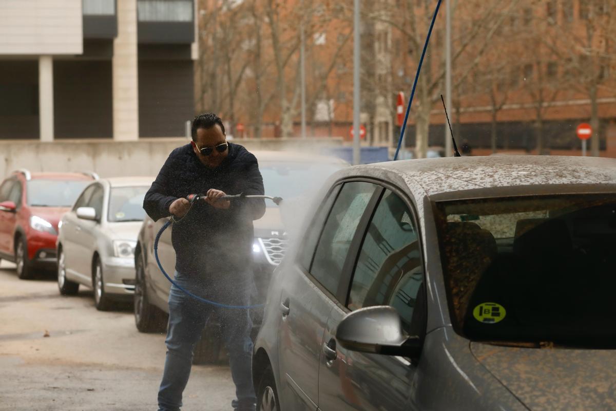 Un hombre lava su vehículo, cubierto por polvo sahariano, en Madrid.