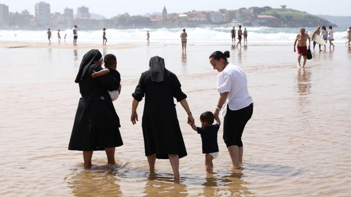 Dos monjas con unos niños y una cuidadora, en San Lorenzo, en Gijón, en cuya costa se aprecia el polvo en suspensión. | Juan Plaza