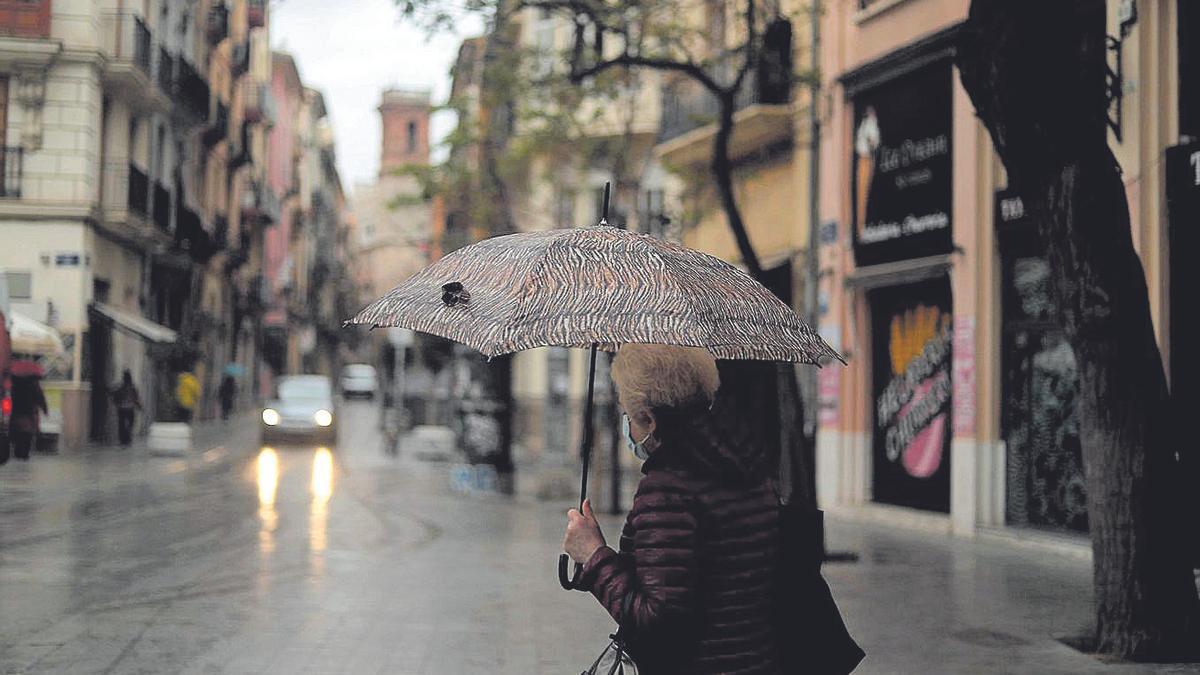Una mujer se resguarda bajo su paraguas mientras llueve en el centro de València.