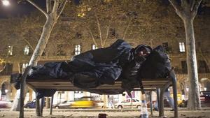 Una persona sense sostre dorm en un banc al costat de la Ciutadella.