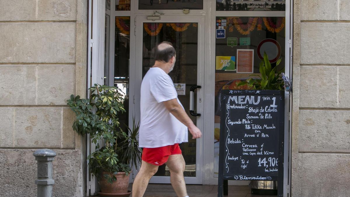 Un hombre mira un cartel de menú de un restaurante de la calle San Fernando de Alicante.