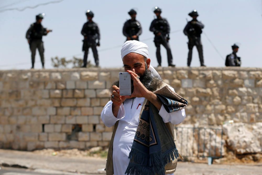 Un hombre palestino mira en su teléfono móvil mientras los oficiales de policía fronterizos israelíes se paran en una pared detrás de él en una calle fuera de la Ciudad Vieja de Jerusalén.