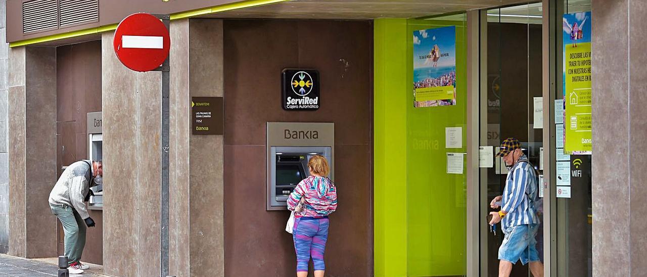 Varias personas hacen uso de un cajero de Bankia en la calle La Naval de la capital gran canaria .