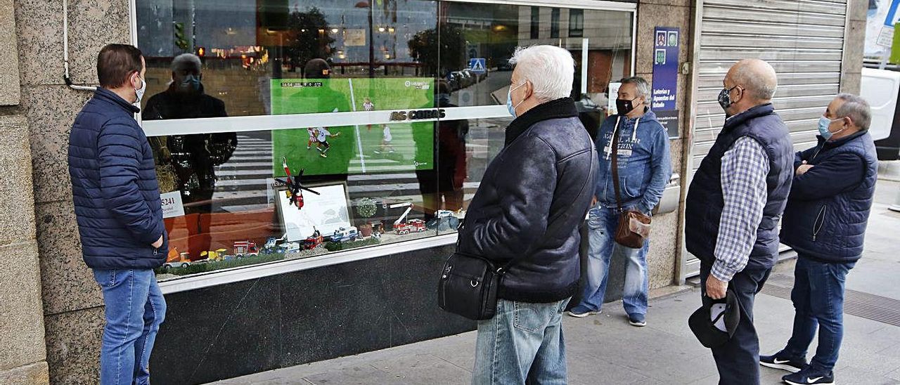 Vecinos de O Calvario ven desde fuera un partido puesto en la tele del bar As Cobas