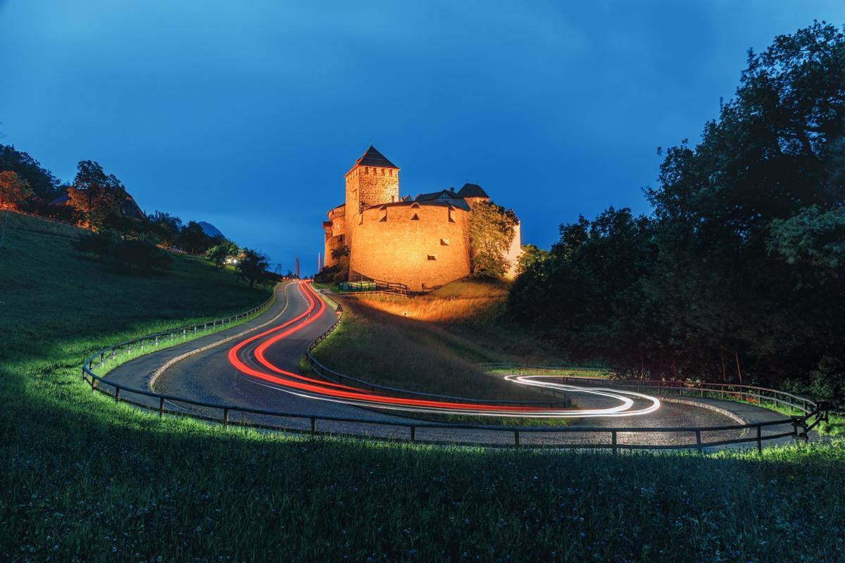 El imponente castillo de Vaduz se ilumina al anochecer, custodiando la capital, Vaduz, desde su privilegiada posición en lo alto de la montaña.