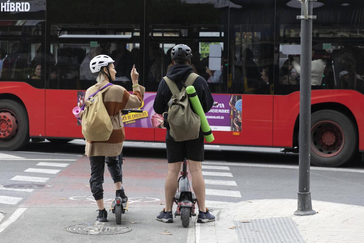 Dos usuarios de patinetes esperan a que pase el bus de la EMT por el carril bici.