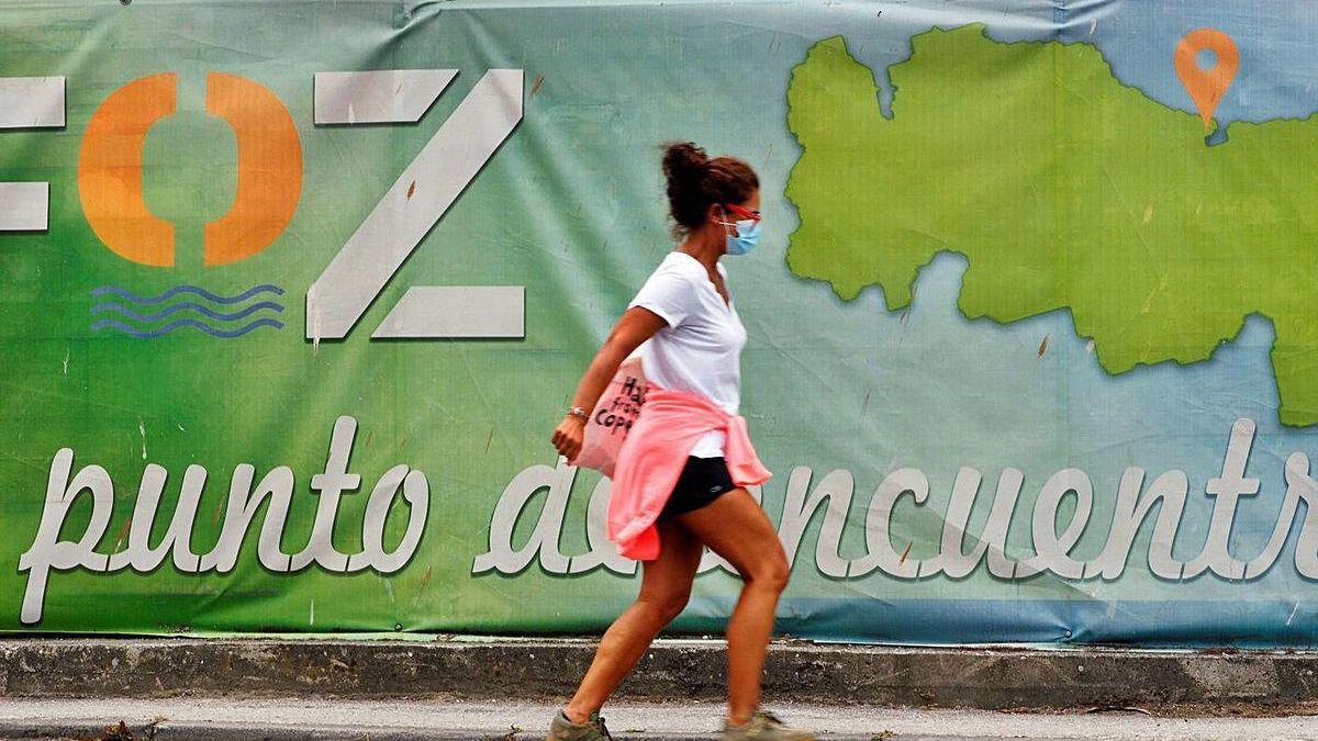 Una mujer con mascarilla camina ante un cartel publicitario de Foz, en la Mariña lucense.