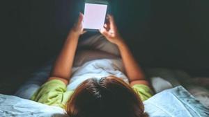 Un niño mirando la pantalla de un móvil en su cama.