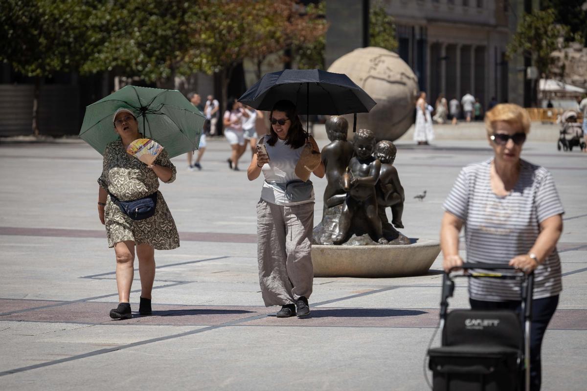 Varias personas pasean con sombrillas por el centro de Zaragoza.