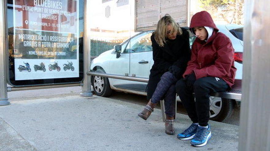 Dues persones en una parada de bus resguardant-se del fred a Roses