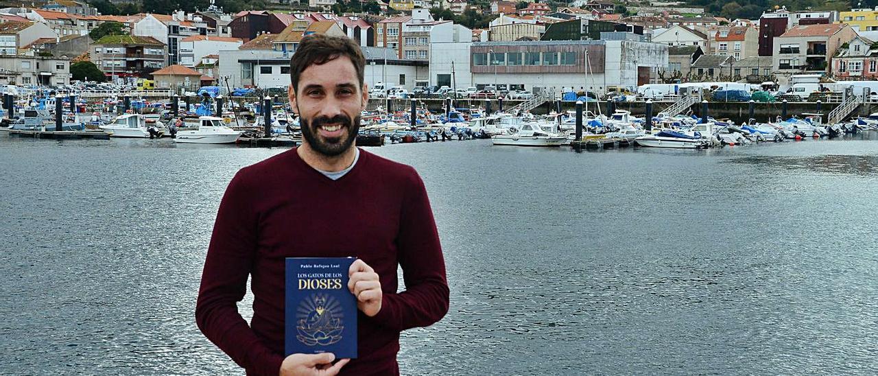 Pablo Refojos posa junto al puerto de Bueu con su novela.   | // GONZALO NÚÑEZ