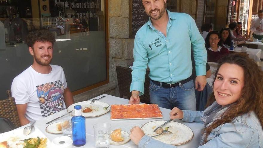 Borjita Martínez sirve el campanu del Sella a los valencianos Daniel García Pujades y Lucía García Gómez, en Cangas de Onís ayer.