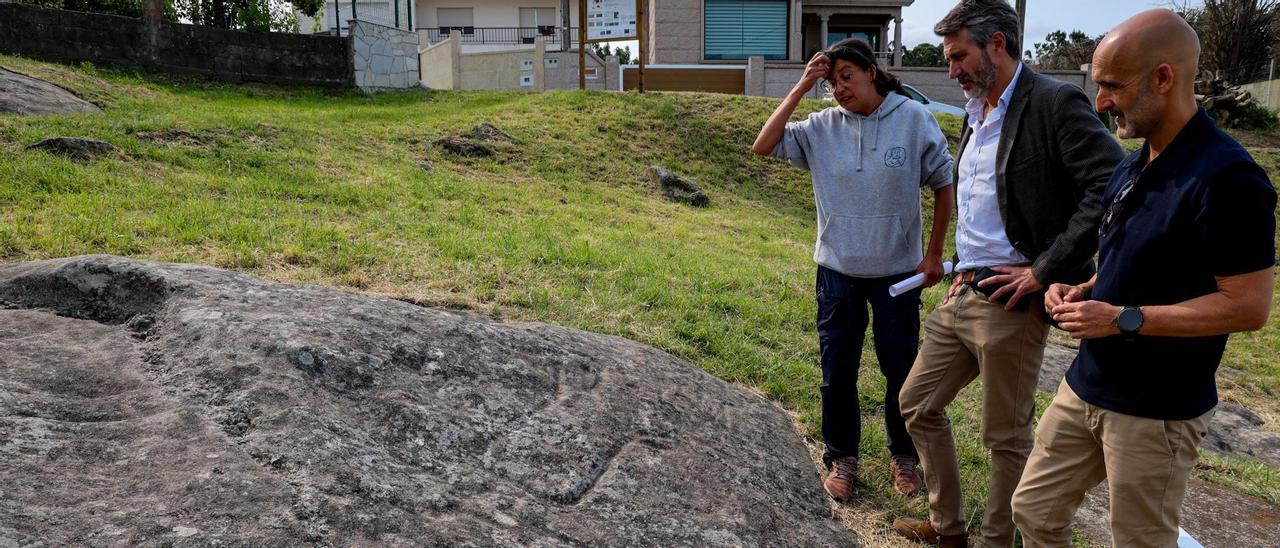 Iria López, Alberto Varela y Álvaro Carou observan una roca con grabados en Os Ballotes.