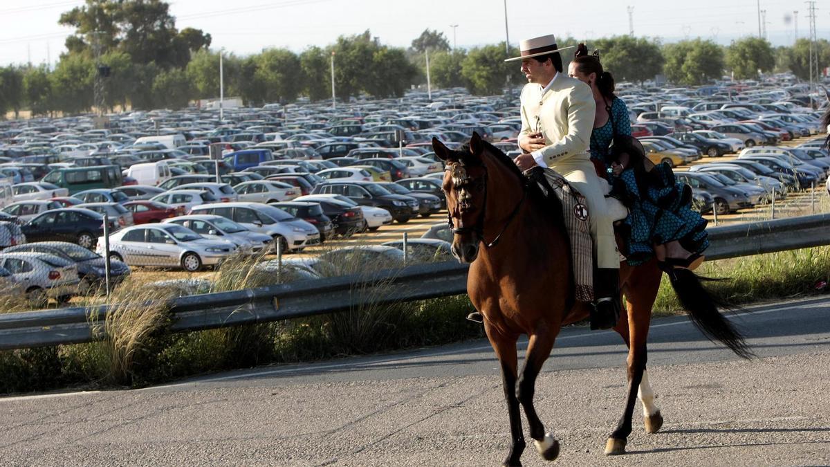 Una pareja se dirige hacia la Feria de Abril a lomos de un caballo, junto a uno de los aparcamientos habilitados para esta fiesta. / Paco Cazalla