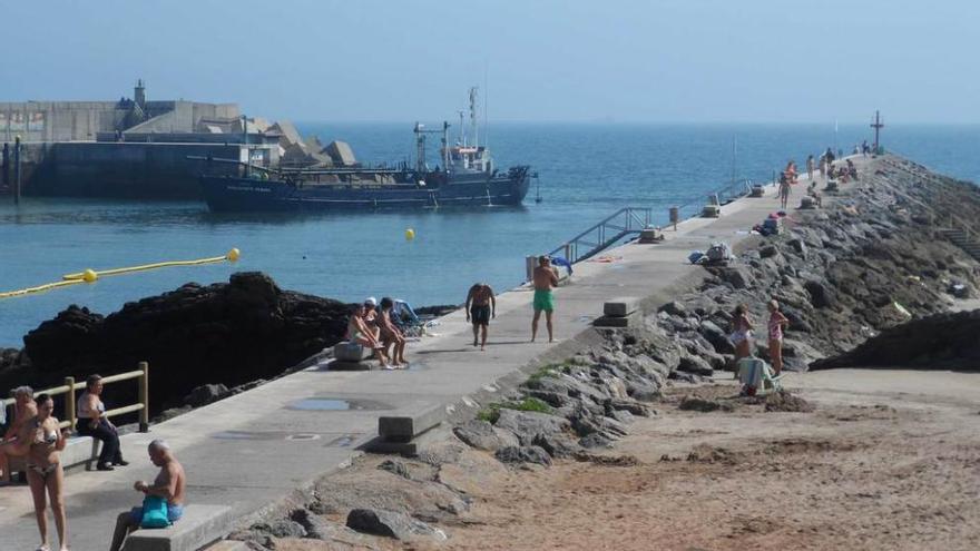 Bañistas en la playa Palmera, con la draga trabajando al fondo, en la bocana del puerto de Candás.