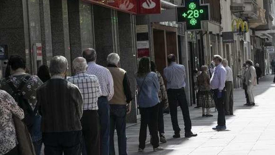 Un termómetro señala 28 grados en Oviedo mientras vecinos hacen cola para acceder a una entidad bancaria.