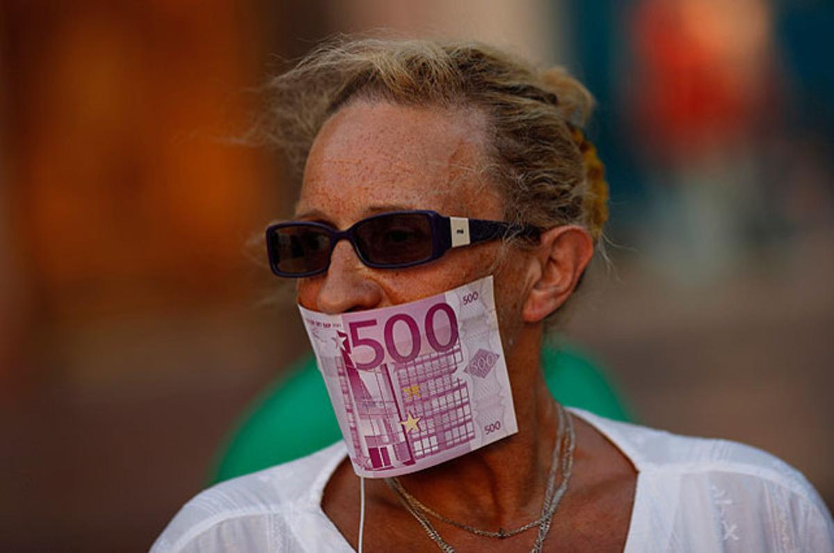 Una dona cobreix la seva boca amb una bitllet  fals durant una protesta realitzada a la plaça de la Constitució de Màlaga contra el pla de rescat d’Espanya. Els  ministres de l’Eurozona han acordat prestar fins a 100 milions d’euros a Espanya per salvar el sistema financer.
