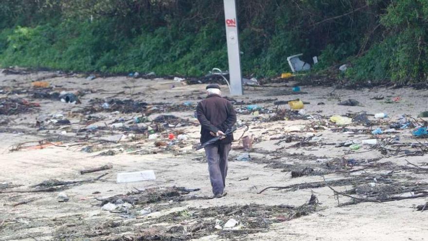 Una persona pasea por la playa de Cesantes llena de basura que arrastró el mar durante el temporal. // R.G.
