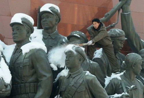 Man brushes snow off the top of a monument at Mansudae in Pyongyang