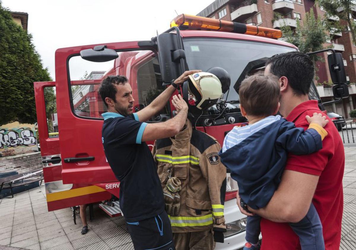 Un bombero muestra el traje de faena a un padre y a su hijo. | Irma Collín