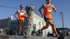 Los atletas pasan la polémica barrera de separación de Israel, que divide a Cisjordania de Jerusalén, en la ciudad bíblica de Belén, en la ocupada Cisjordania, durante la séptima maratón internacional de Palestina.