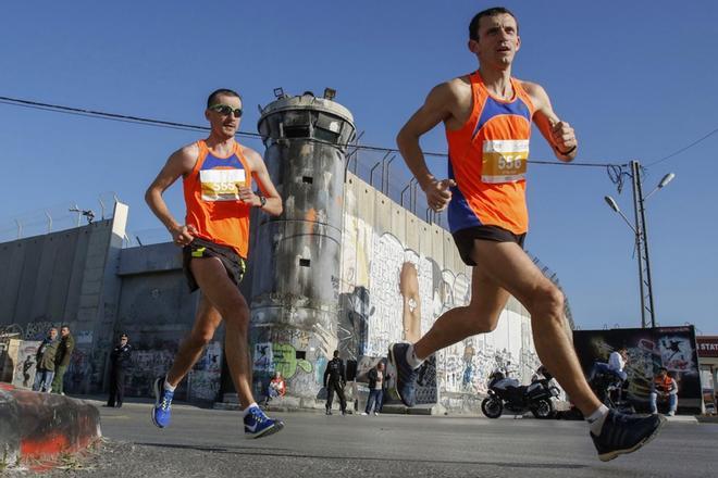 Los atletas pasan la polémica barrera de separación de Israel, que divide a Cisjordania de Jerusalén, en la ciudad bíblica de Belén, en la ocupada Cisjordania, durante la séptima maratón internacional de Palestina.