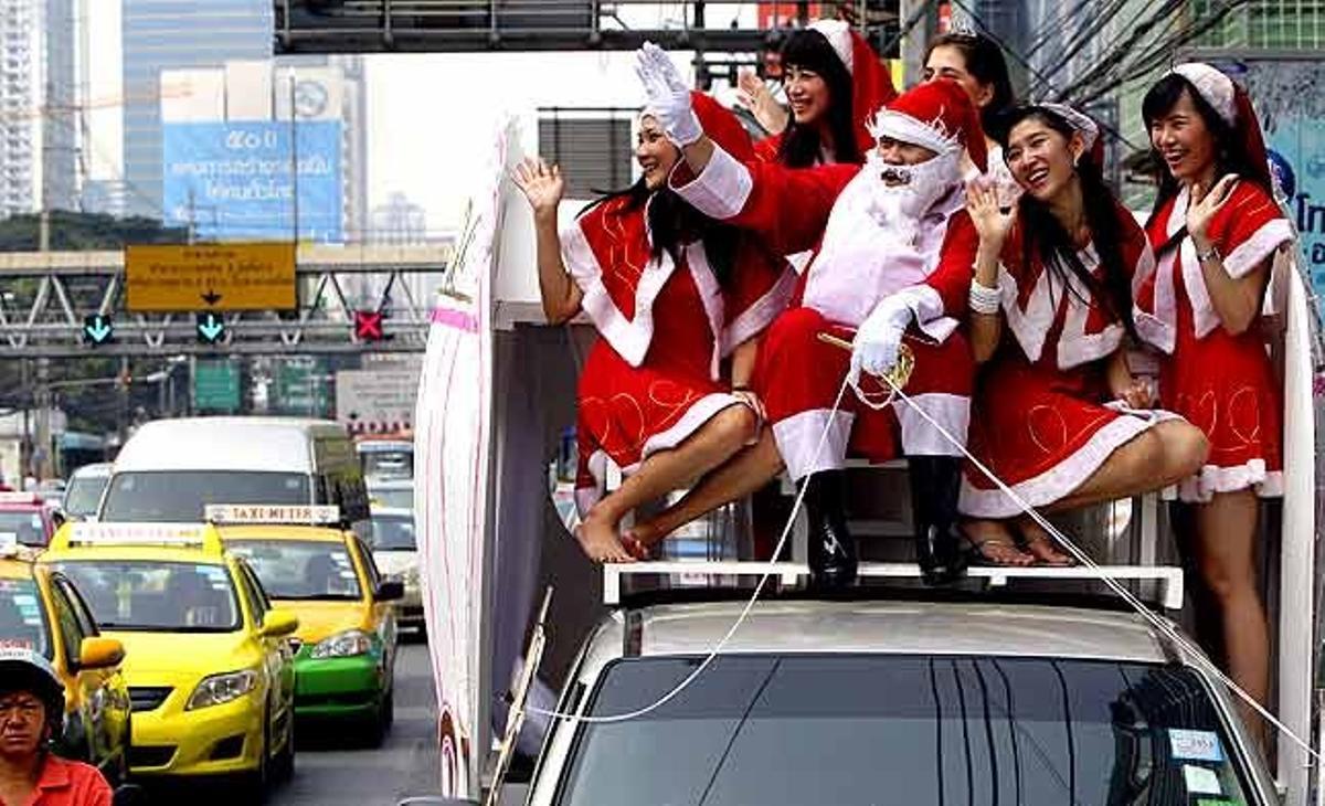 Empleats d’un hotel disfressats de Santa Claus i de Santalady saluden els conductors des del sostre d’una furgoneta decorada com una carrossa. Durant el recorregut van repartir galetes a vianants i turistes, al centre de Bangkok (Tailàndia).