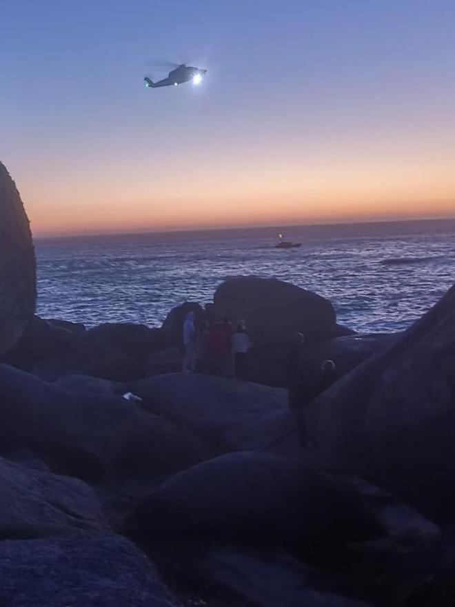 Uno de los helicópteros y una de las lanchas participantes, cuando ya anochecía. Entre las rocas se aprecia a algunos ciudadanos que también buscan.