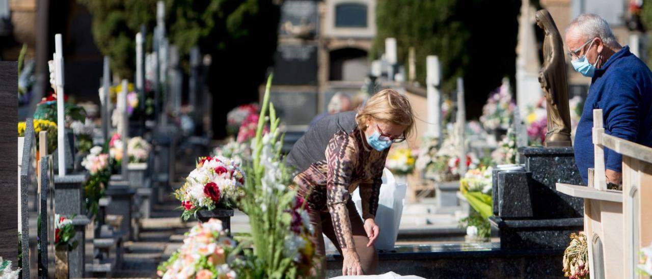 Dos personas depositan flores en una tumba en el cementerio de Alicante.