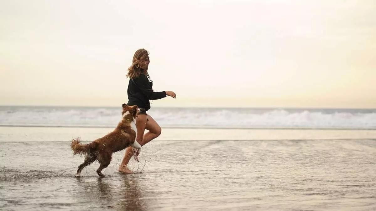 Una mujer corre con su perro por la orilla del mar.