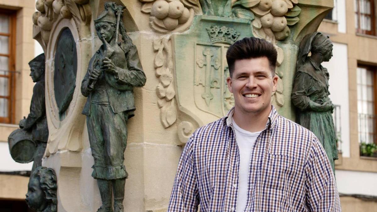 Alejandro Zurbriggen posa junto al gaitero tallado en la peana de la escultura "La Manzanera", en Villaviciosa.