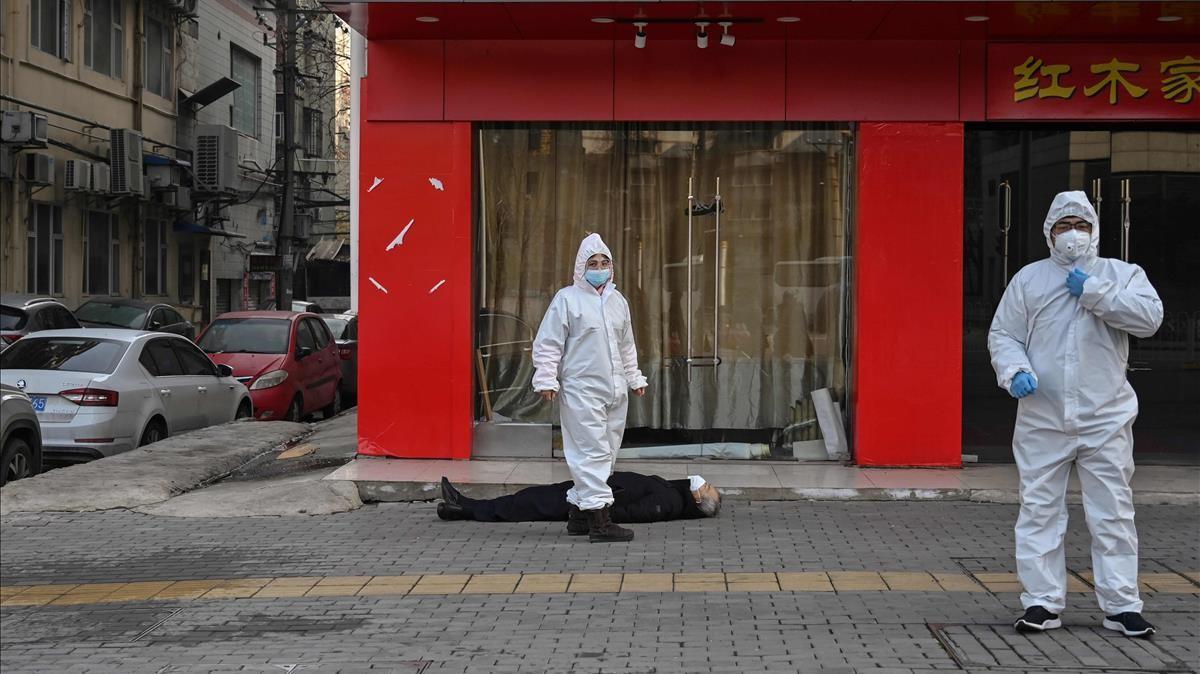 Funcionarios con trajes de protecci&oacute;n controlando a un anciano con una mascarilla que se derrumb&oacute; y muri&oacute; en una calle cerca de un hospital en Wuhan, el 30 de enero de 2020