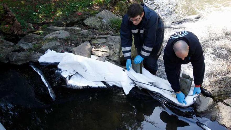 Operarios forman un dique con mantas absorbentes para evitar que el vertido se extienda al cauce.  // R. Grobas