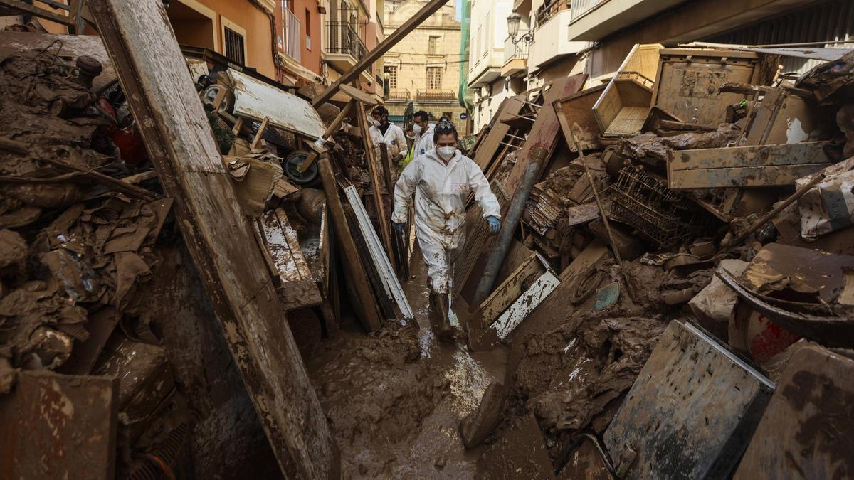 Varios voluntarios atraviesan un pasillo de escombros y basura en Paiporta