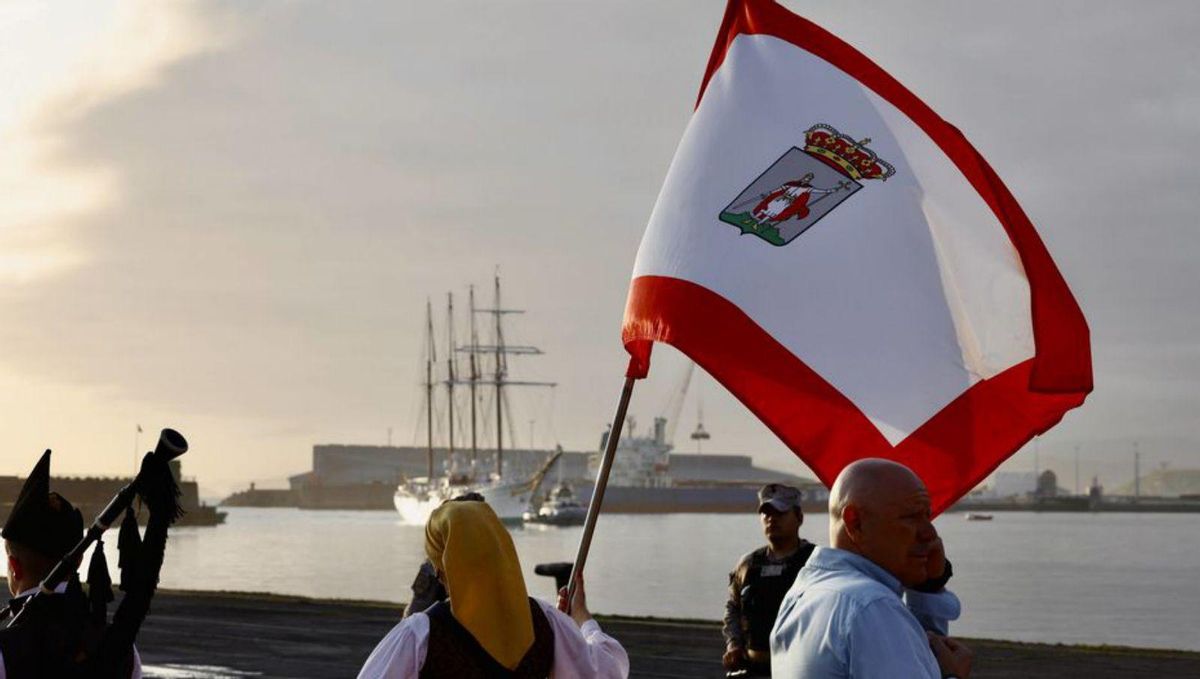 Una componente de la banda «Saxum» porta la bandera de Gijón con el «Juan Sebastián de Elcano» al fondo.