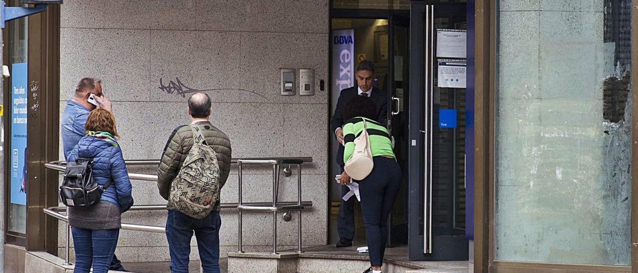 Unas personas esperan su turno para entrar a una oficina bancaria durante el confinamiento.