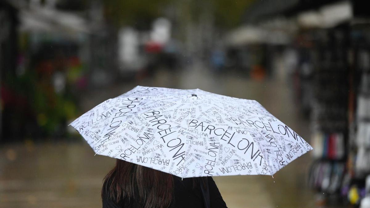 Un paseante se protege de la lluvia bajo su paraguas en las Ramblas.