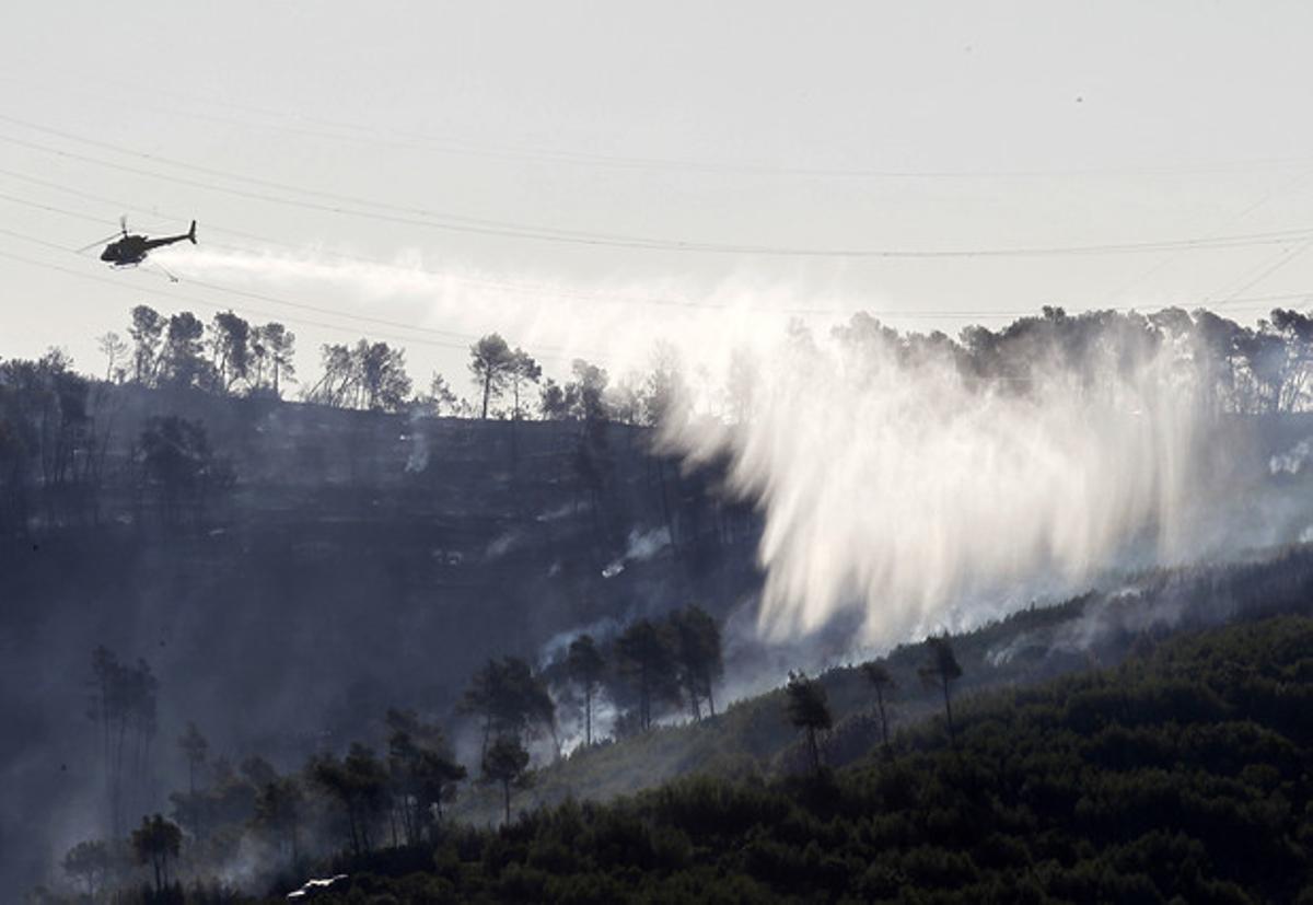 Un helicòpter continua amb les tasques d’extinció de l’incendi de Vallirana aquest dilluns.
