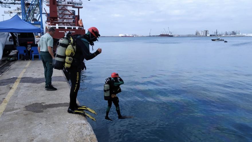 Dos buzos de la Guardia Civil se lanzan al mar en busca del estibador aún desaparecido.