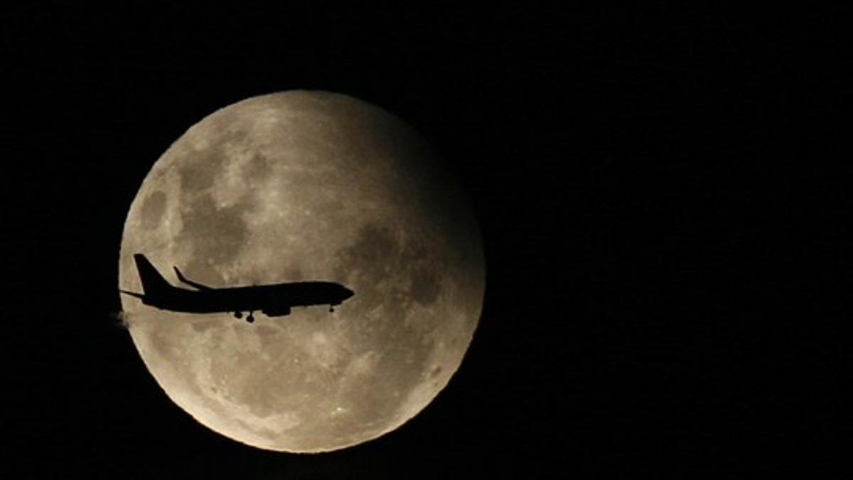 Un avión de pasajeros vuela, con la Luna de fondo, durante el transcurso de un eclipse parcial.