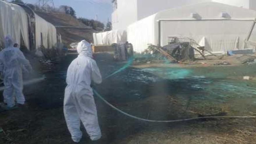 Trabajadores riegan resina verde a base de polvo protector en el área de una piscina dañada en la planta nuclear de Fukushima.