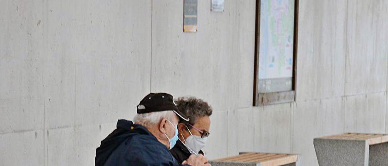 Dos personas mayores en un banco, ante la plaza de Bueu. |   // G.N.