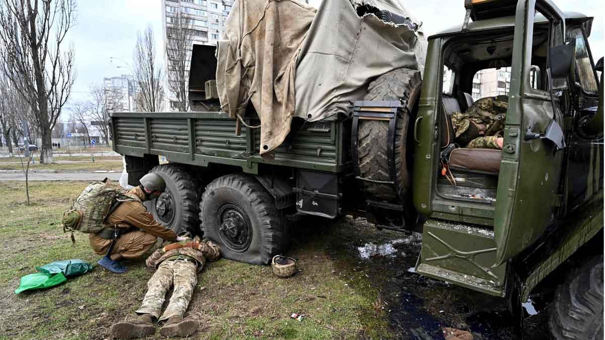 Un médico militar ucraniano examina el cuerpo de un soldado ruso vestido con un uniforme militar de Ucrania, junto a un camión militar, tras una escaramuza en Kiev. Dentro del vehículo yace otro cuerpo.