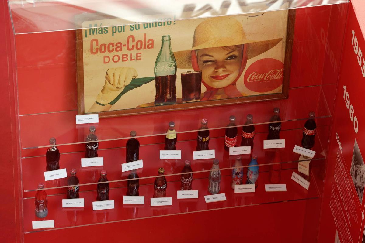 Colección de botellas de Coca Cola junto a un cartel publicitario protagonizado por Carmen Sevilla, en los años 60.