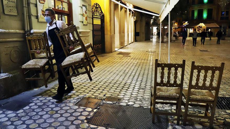 Un empleado recoge, justo antes del toque de queda, la terraza de un establecimiento hostelero situado en  el centro de la capital malagueña.