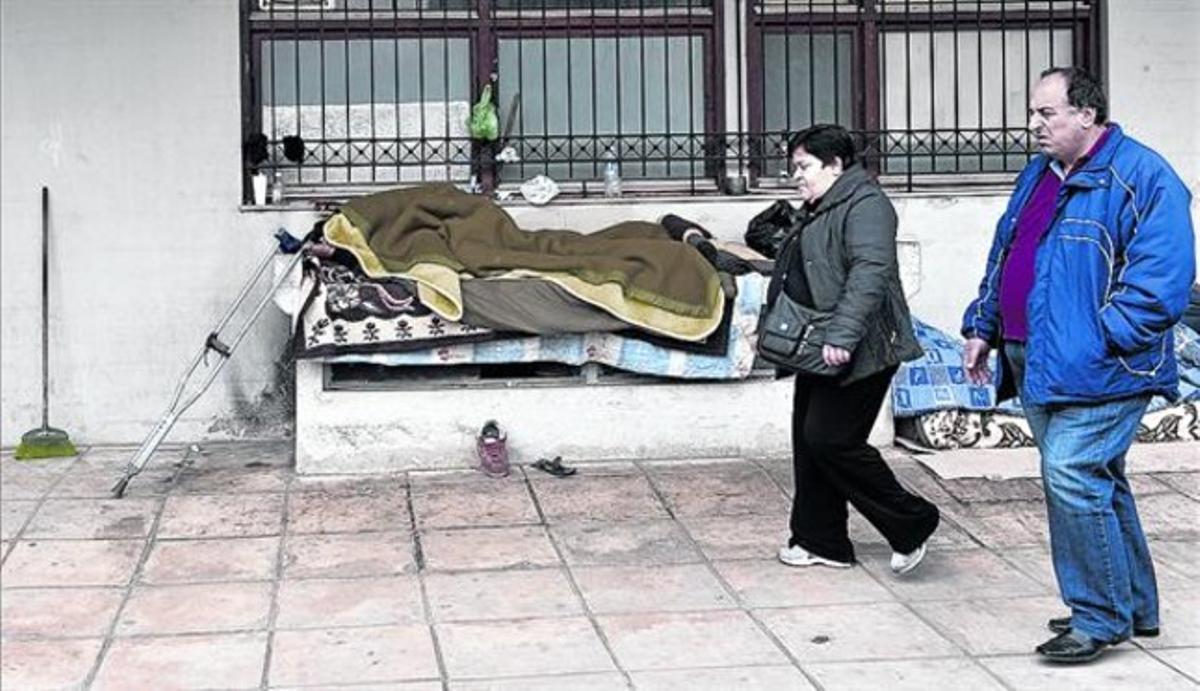 Dos ciutadans passen pel costat d’un sense sostre que dorm en un banc, a Salònica, ahir. Dos ciutadans passen pel costat d’un sense sostre que dorm en un banc, a Salònica, ahir.