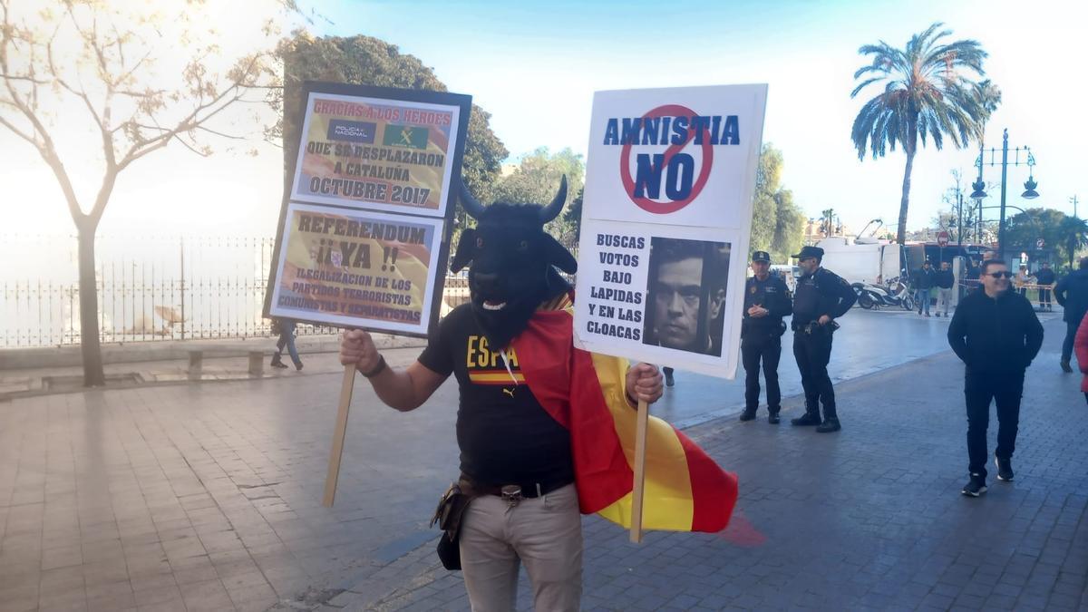 Un simpatizante del PP portada dos carteles contra Pedro Sánchez al tiempo que luce una cabeza de toro.